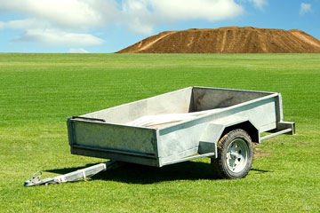 an empty utility trailer parked on a green meadow